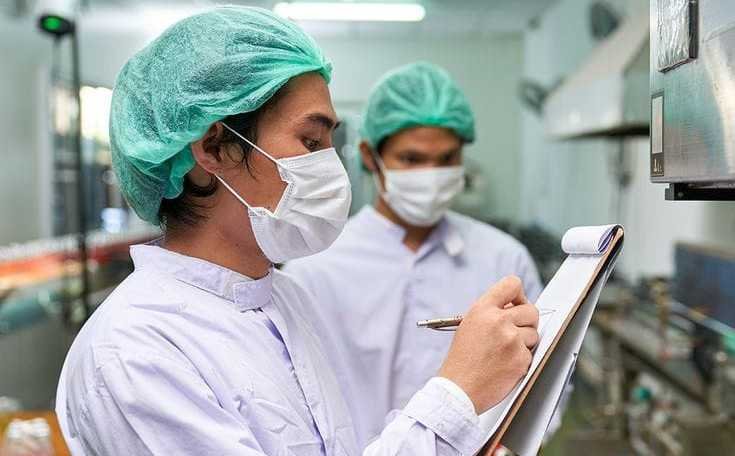 una mujer y un hombre en un laboratorio, ella tiene una tabla con un documento en la mano y un bolígrafo en la otra